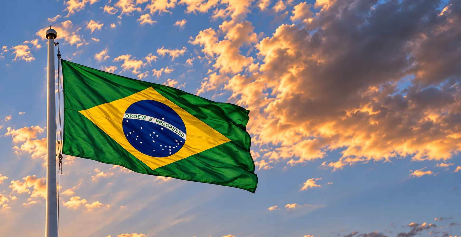 Bandeira do Brasil ao vento no alto do mastro, contra nuvens de fim de tarde